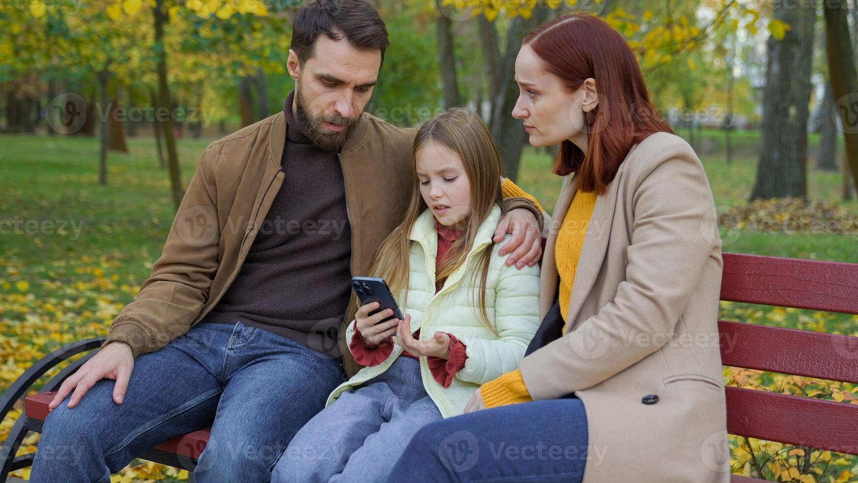 Caucasian family at city bench together outdoors autumn sad upset confused worried with mobile phone bad news smartphone failure little daughter girl child kid with parents mother woman father man photo