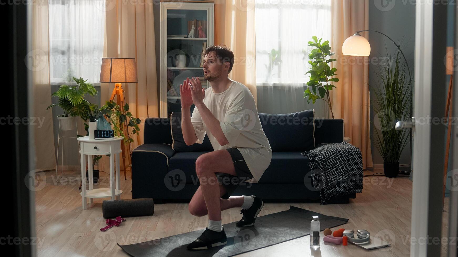 Active sporty strong Caucasian man fitness male athletic sportsman young guy doing forward lunges sport exercise training legs workout squats bodycare healthy lifestyle indoors apartment living room photo