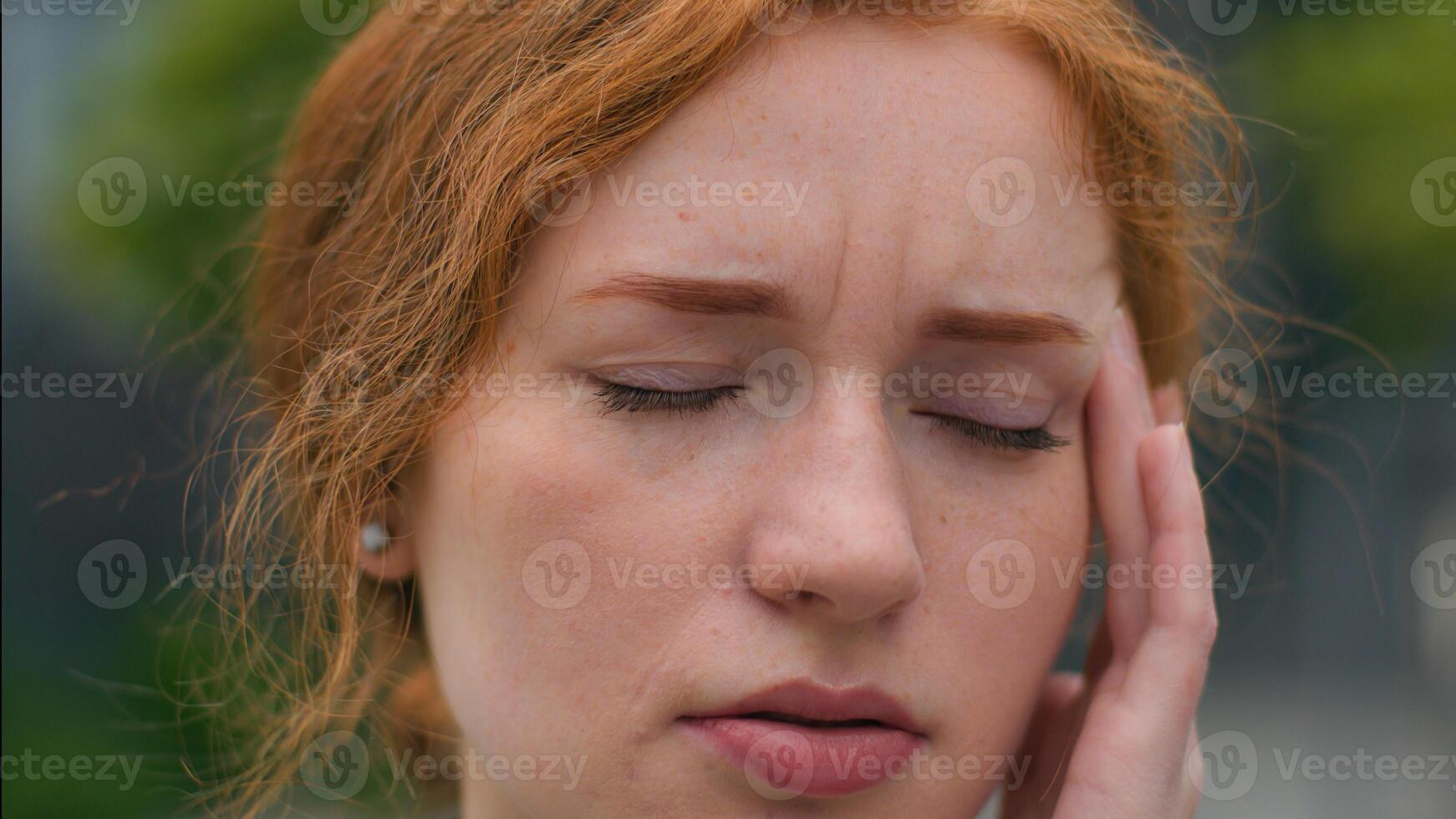 Close up young unhealthy professional employee Caucasian ginger girl businesswoman lady female woman feels unwell fever headache panic attack eyes closed massaging temple head hand outside city street photo