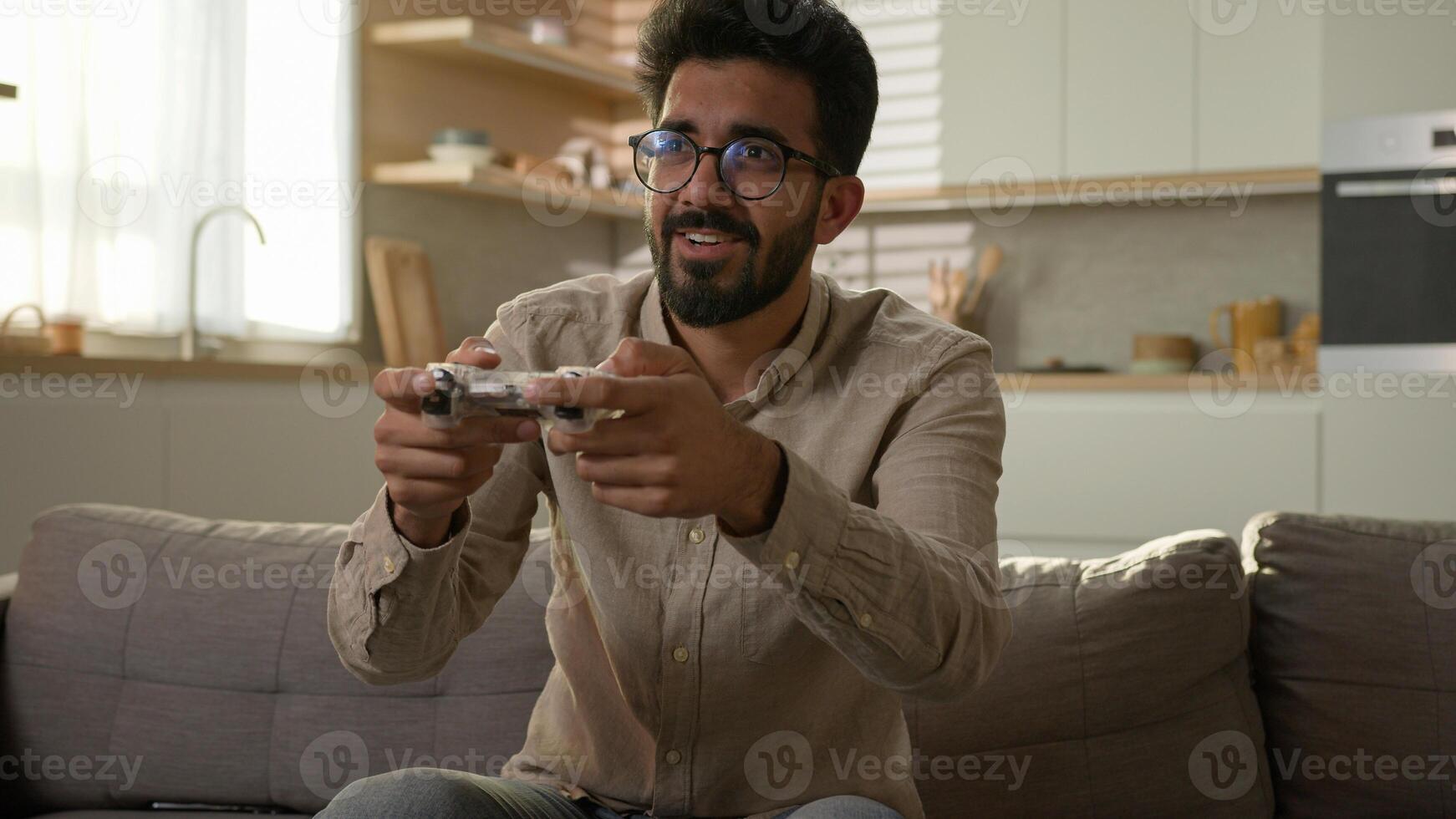 Indian Arabian man ethnic guy have fun on sofa couch play online game smart TV console virtual driving car use wireless controller entertainment in home kitchen male gamer playing with joystick photo