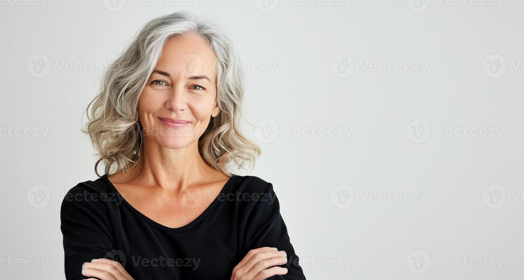 Waist up beautiful smiling middle aged woman with gray hair holding crossed hands on breast looking at camera in black dress on white background photo
