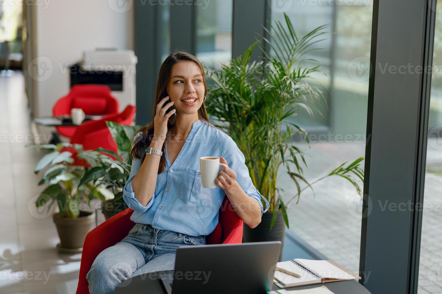 A professional businesswoman is on a call and enjoying coffee in a modern office with a laptop photo