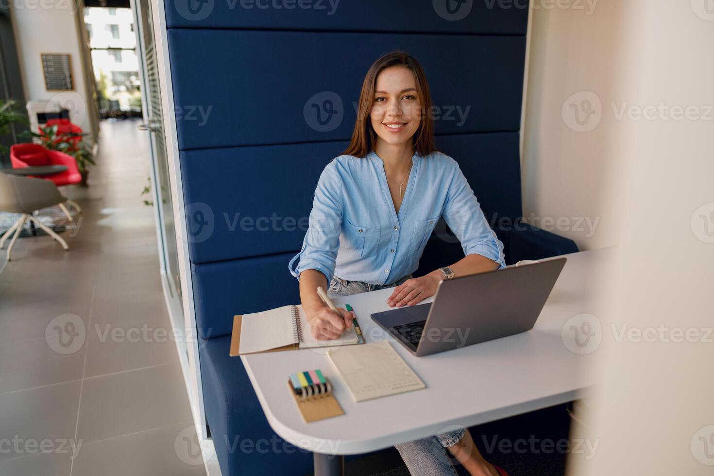 A professional woman is smiling, using a laptop, and taking notes in a modern office environment photo