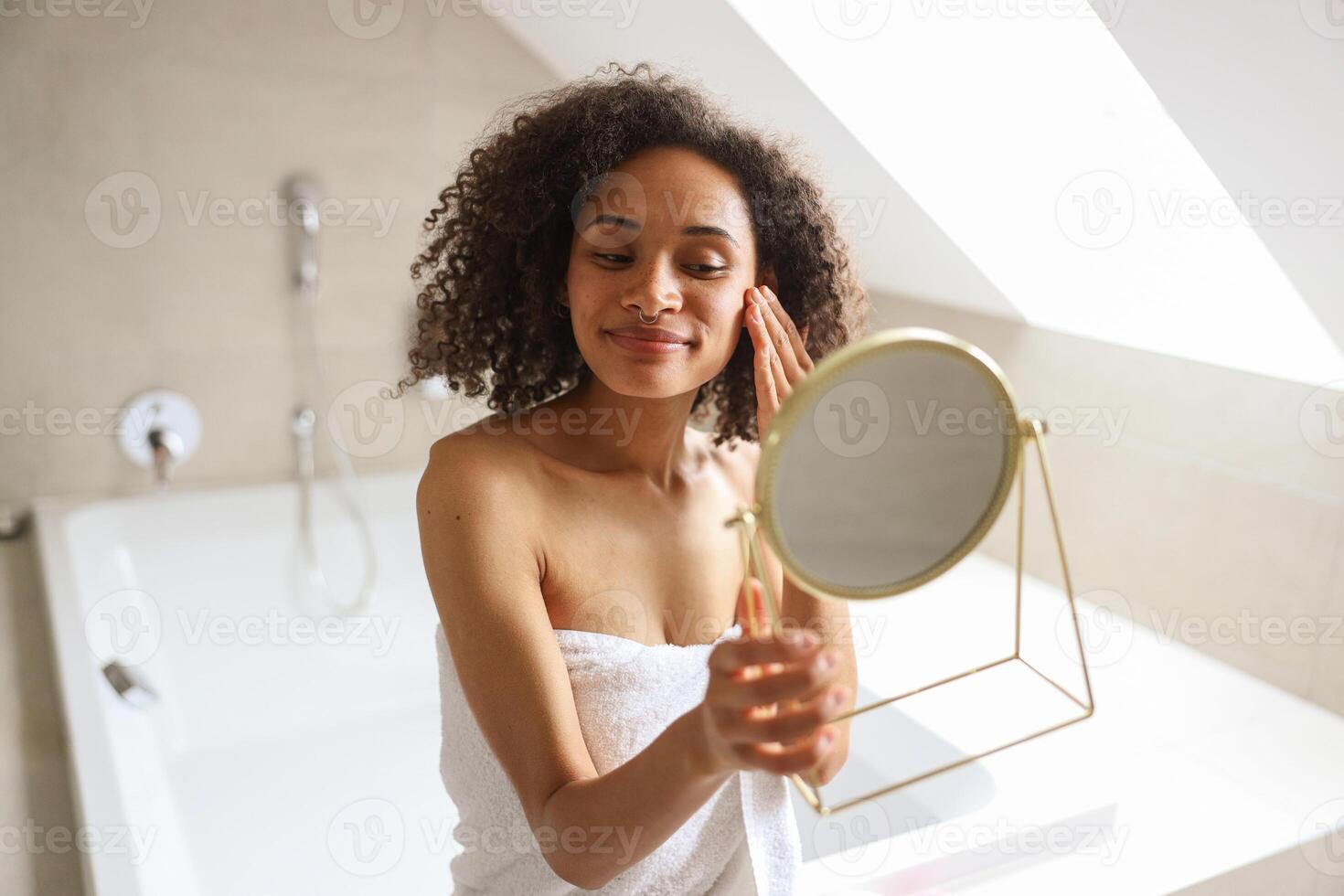 A woman in towel smiles while looking at her reflection in the bathroom mirror photo