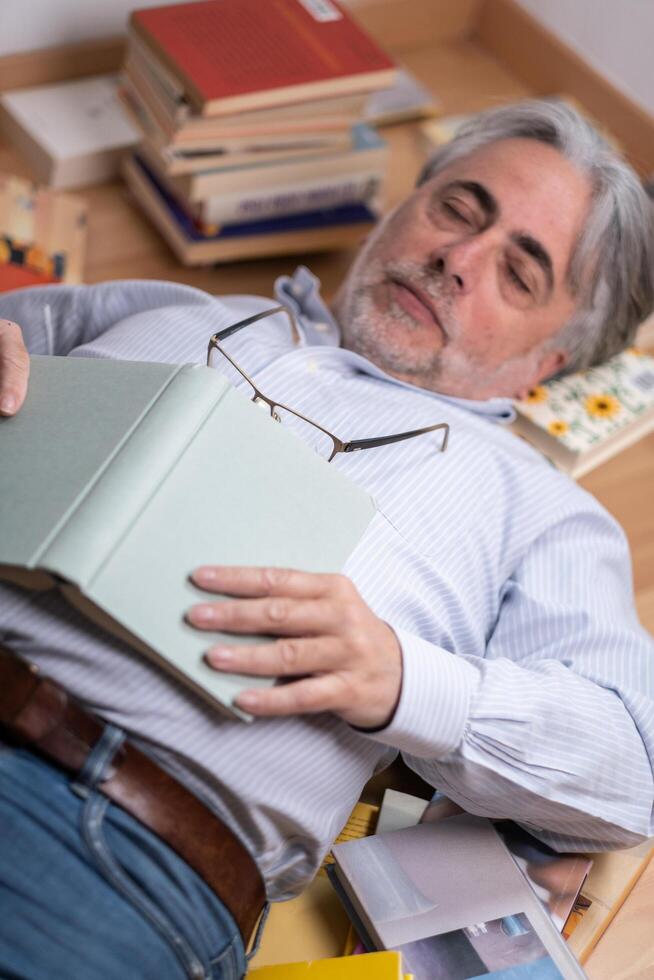 Middle-aged man sleeping among numerous books distributed on the floor. photo