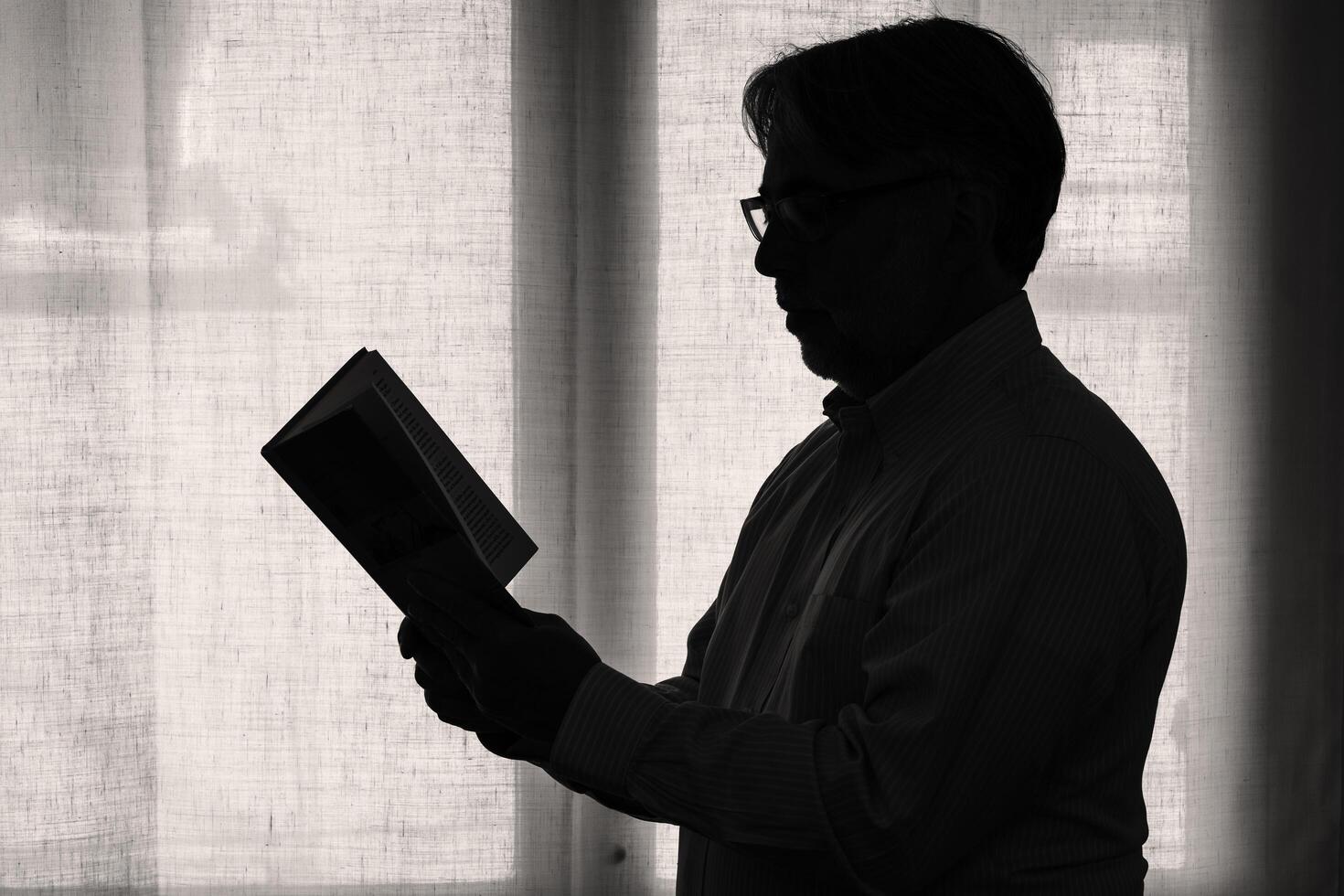 Silhouette of male person reading a book at home near the window. photo