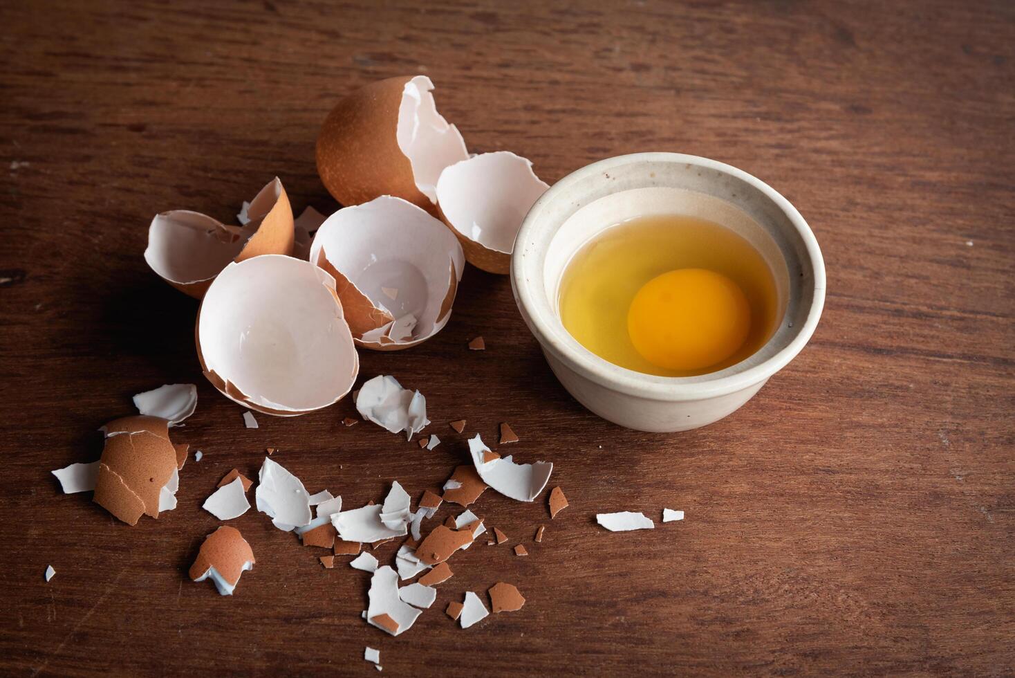 Broken egg shells and eggs on tray and pot, raw egg in small bowl at wooden background menu and recipe photo