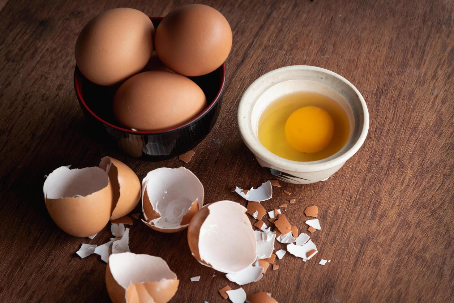 Broken egg shells and eggs on tray and pot, raw egg in small bowl at wooden background menu and recipe photo