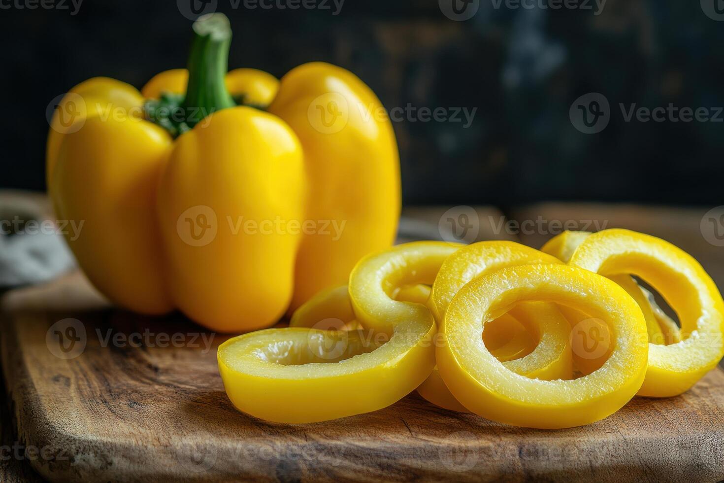 Freshly sliced yellow bell pepper on a rustic wooden cutting board with whole pepper in the background during daylight photo