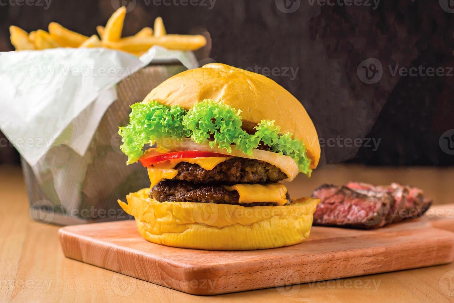 Double Beef Cheeseburger with Lettuce, Jalapeno, Tomato, Cheese, Steak Slices isolated on wooden board with french fries basket side view of fastfood photo