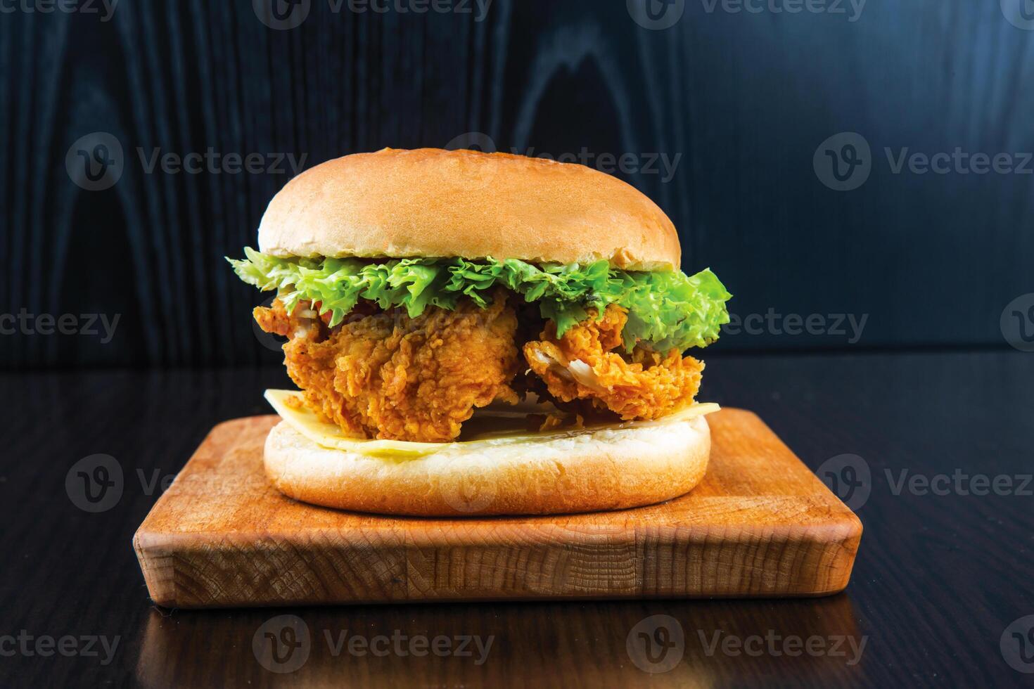 Chicken Zinger Burger with Lettuce, Tomato, Melted Cheese and Sauce isolated on wooden board side view of fastfood on dark background photo