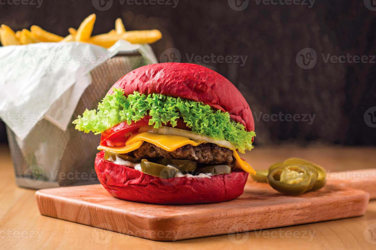 Red Beef Burger with Lettuce, Jalapeno, Tomato, Cheese isolated on wooden board with french fries basket side view of fastfood photo