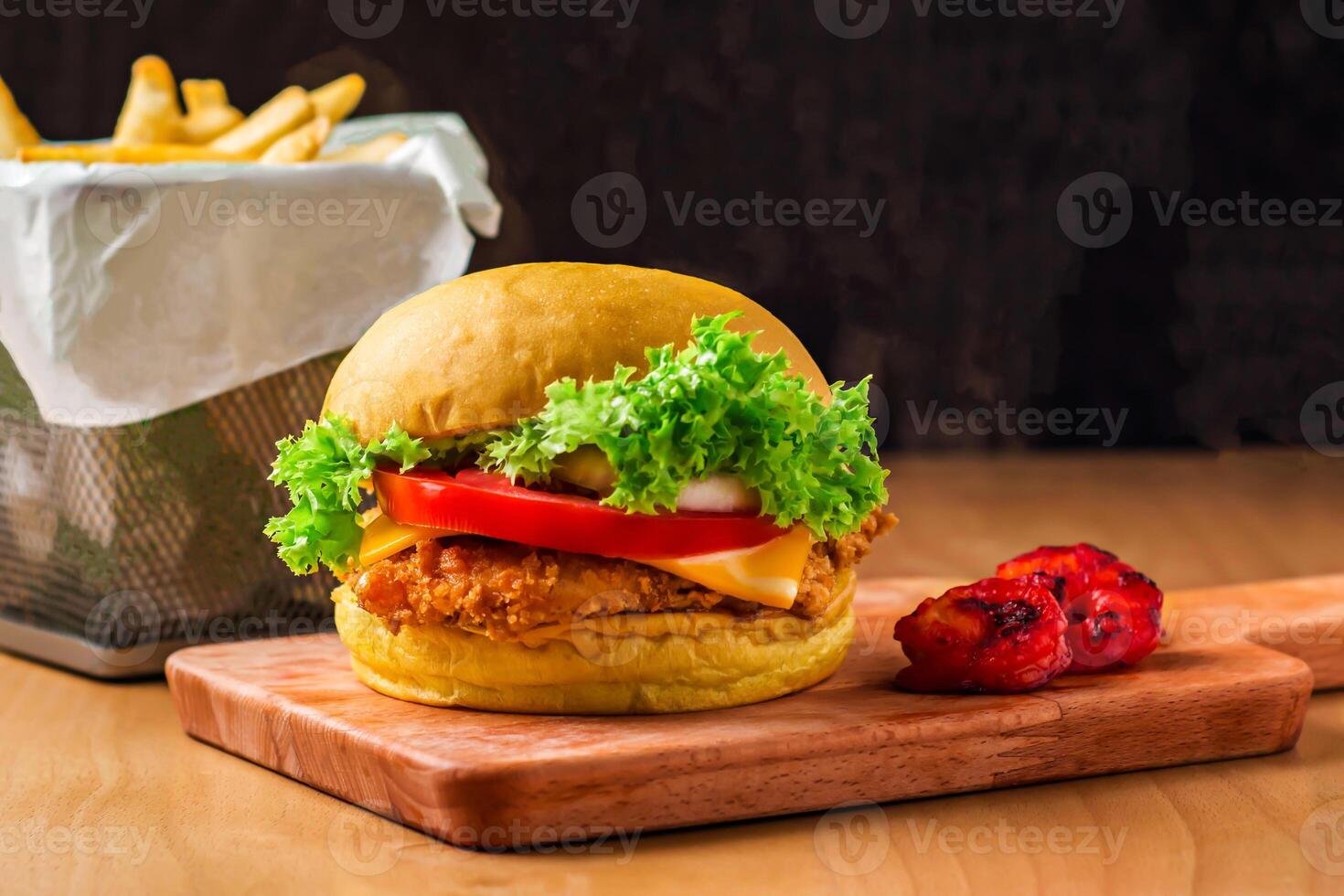Crispy Chicken Burger with Grilled prawn, lettuce, tomato, onion, cheese isolated on wooden board with french fries basket side view of fastfood photo