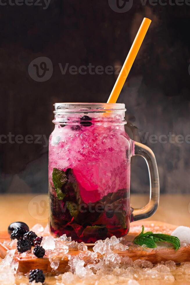 Blackberry Mojito with Mint and Lime served in jar with straw isolated on wooden board side view of perfect drink for a hot summer day photo