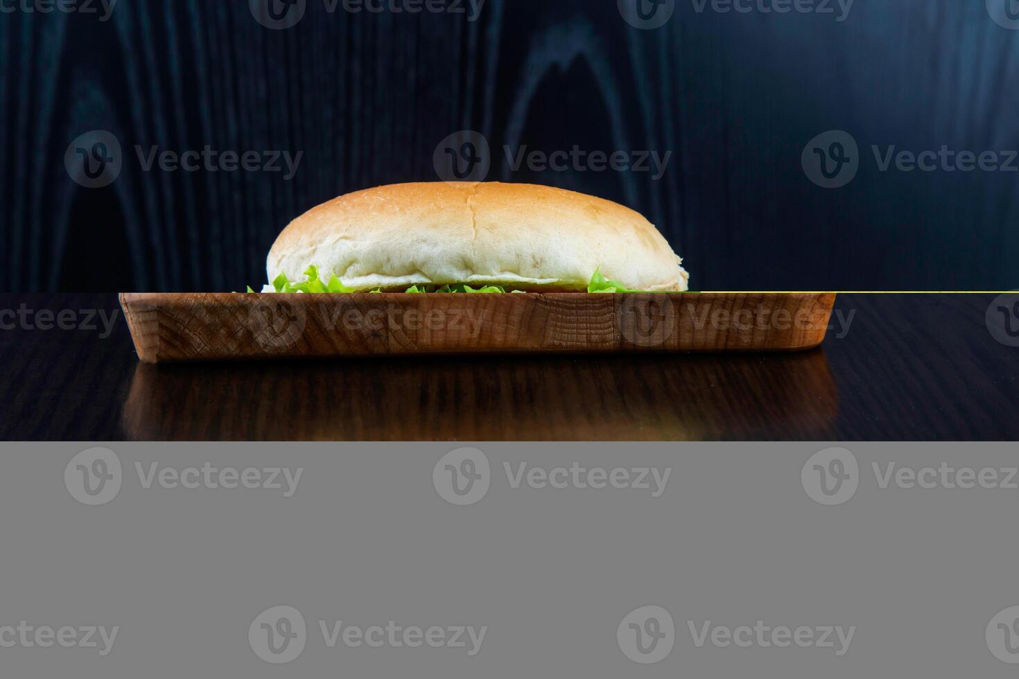 VEGETABLE BURGER with Lettuce, Tomato, and Cheese isolated on wooden board closeup side view of fastfood on dark background photo
