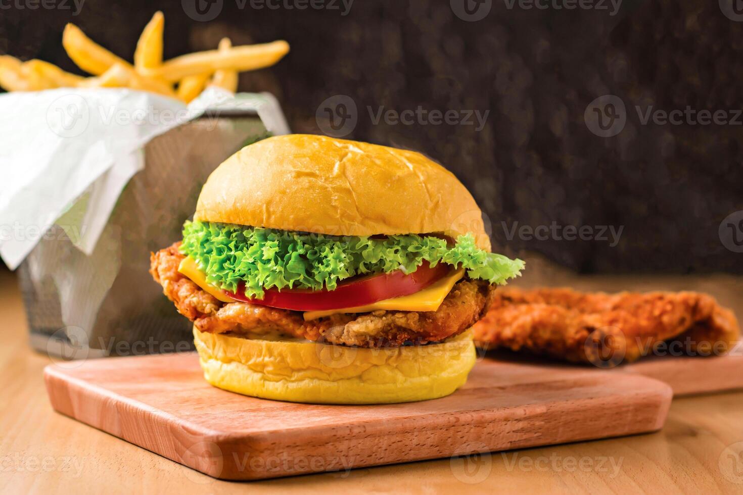 Crispy Chicken Burger with Lettuce, Jalapeno, Tomato, Cheese isolated on wooden board with french fries basket side view of fastfood photo
