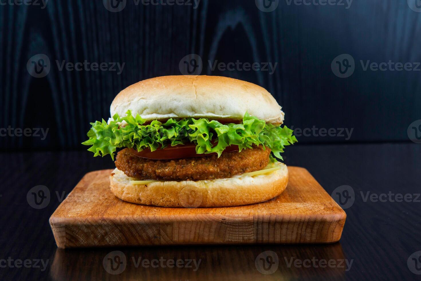 VEGETABLE BURGER with Lettuce, Tomato, and Cheese isolated on wooden board closeup side view of fastfood on dark background photo
