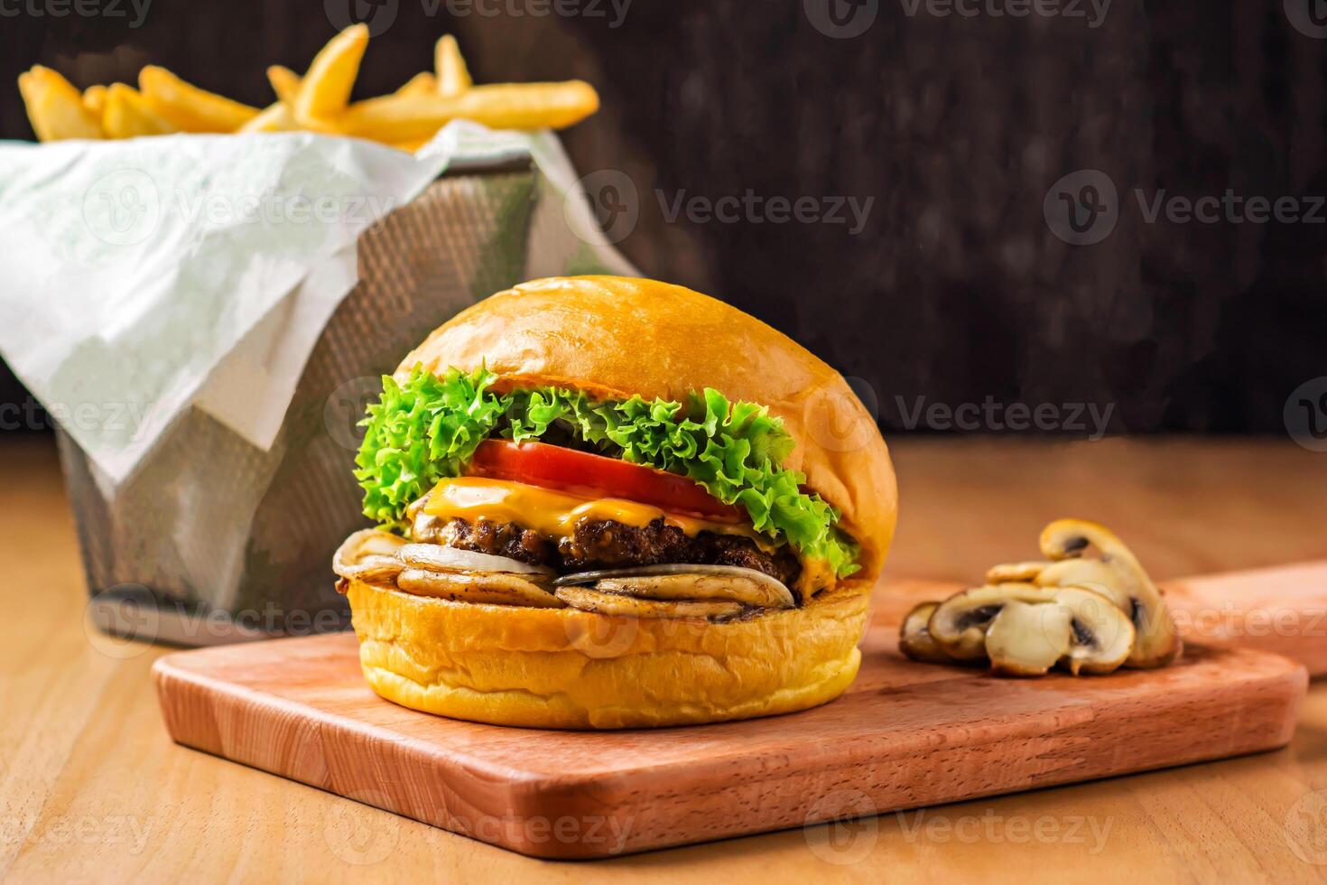 Beef and Mushroom Burger Lettuce, Tomato, Onion and Cheese isolated on wooden board with french fries basket side view of fastfood photo