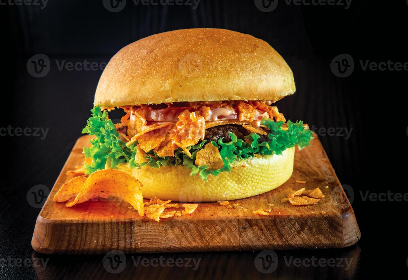 Spicy Loaded Burger with Nacho Cheese and Tortilla Chips topped with melted nacho cheese, crispy tortilla chips, and a spicy sauce isolated on wooden board side view of fastfood photo