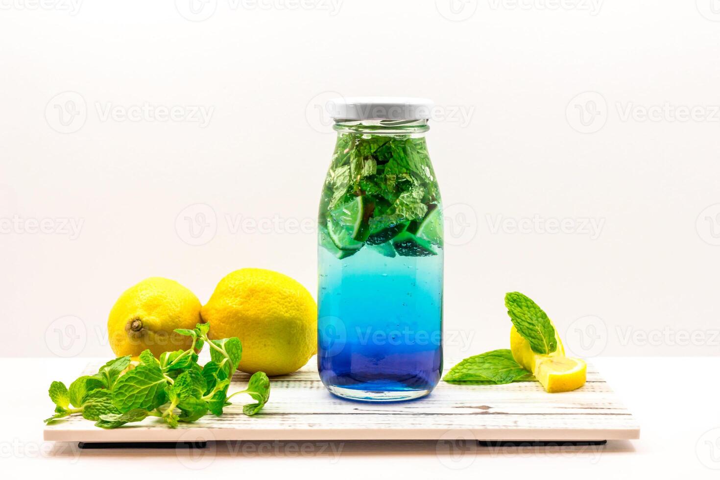Refreshing Blue Lagoon Lemonade with Mint and Lemon served in bottle isolated on wooden board side view of cold beverage on white background photo
