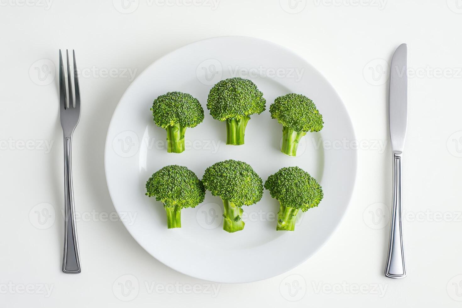 Fresh green broccoli arranged neatly on a white plate with cutlery on a light background photo