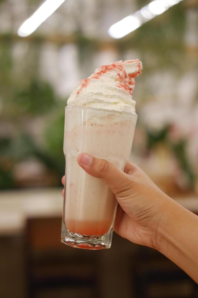 Woman holding a glass of strawberry milkshake with whipped cream. photo