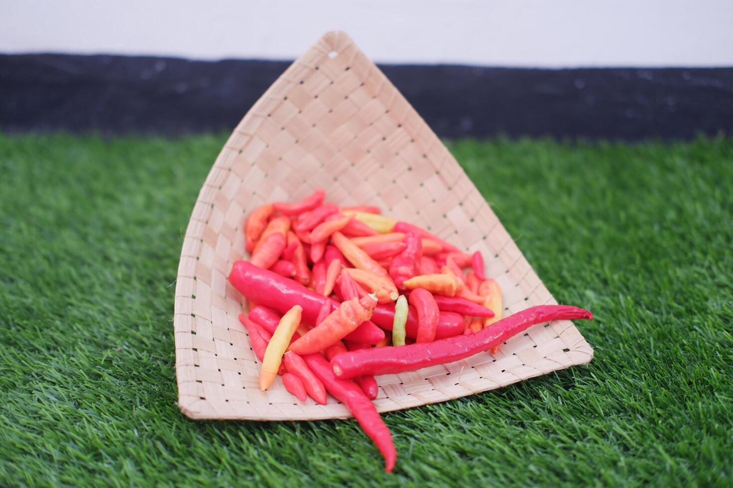Red and yellow chilli in basket on green grass photo