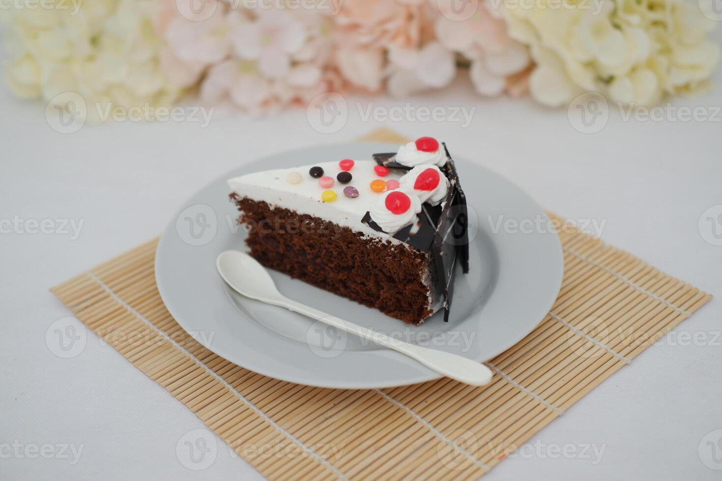 A piece of cake on a white plate with a spoon on a bamboo mat photo