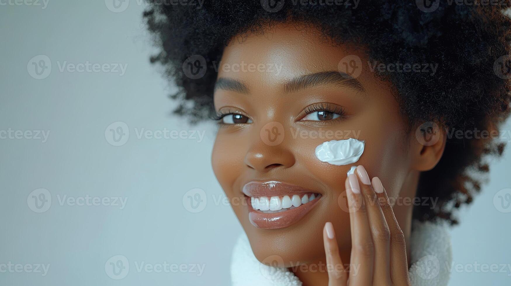 Advertisement image of a Black woman with flawless skin, softly smiling as she applies a moisturizing cream to her cheek with her fingertips, set against a clean, neutral gray background, perfect photo