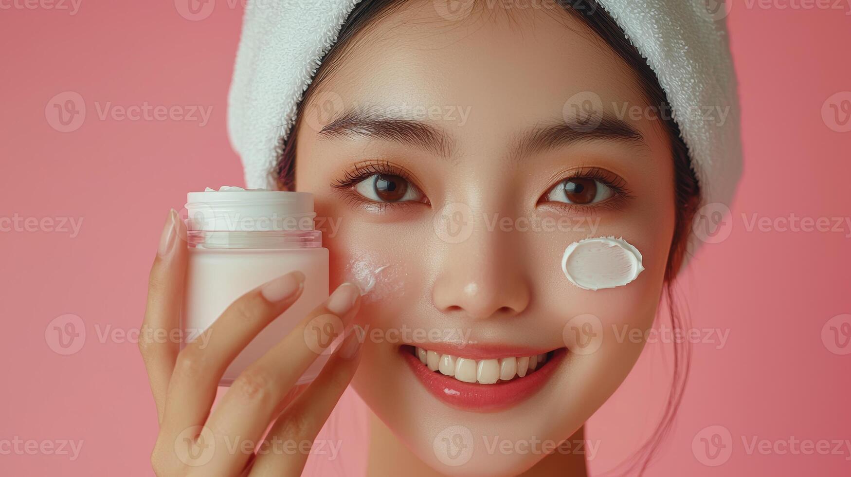 Commercial-style close-up of a young Southeast Asian woman with a bright smile, her hair wrapped in a white towel, holding a jar of cream over one eye while dabs of cream are applied to her photo