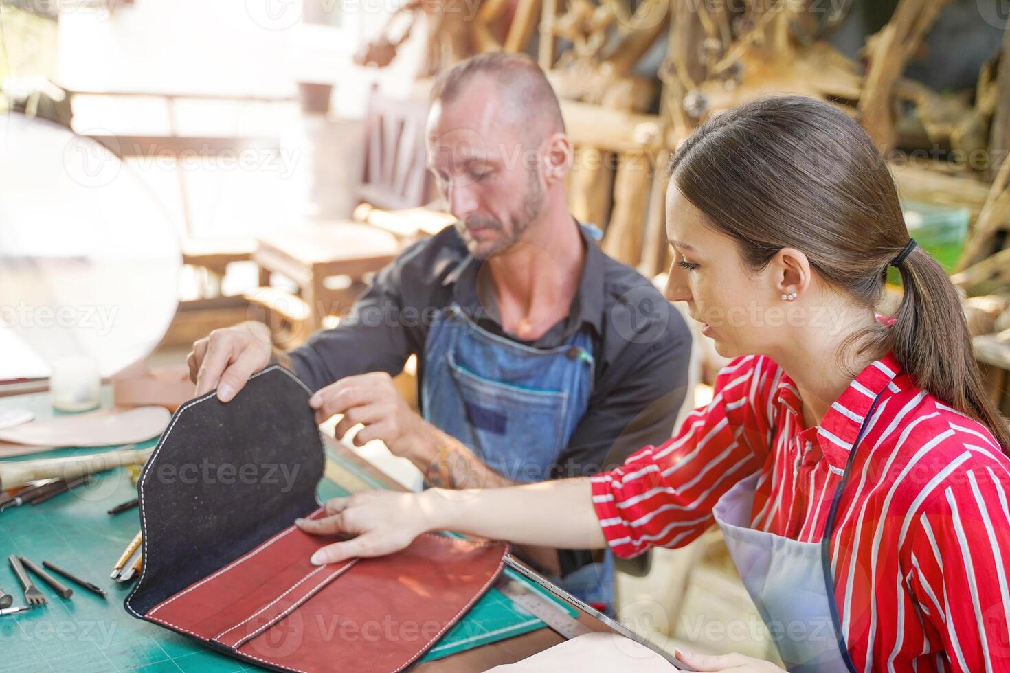Young female leather maker with craftsman looking and checking the neatness of the leathers bag before sell to customer in workshop. photo