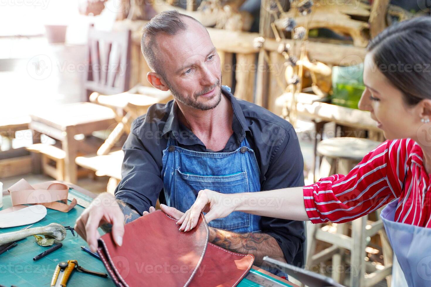 Young female leather maker with craftsman looking and checking the neatness of the leathers bag before sell to customer in workshop. photo