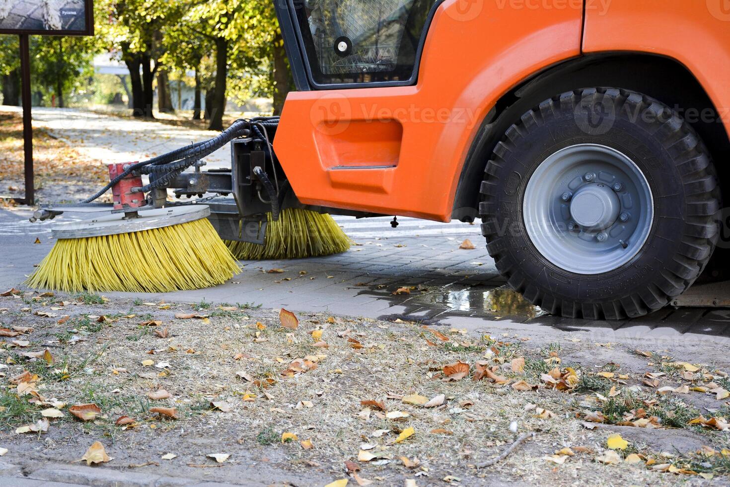Circular brush of a street sweeper machine. Road sweeping by a truck. Electric street cleaner vehicle in the autumn photo