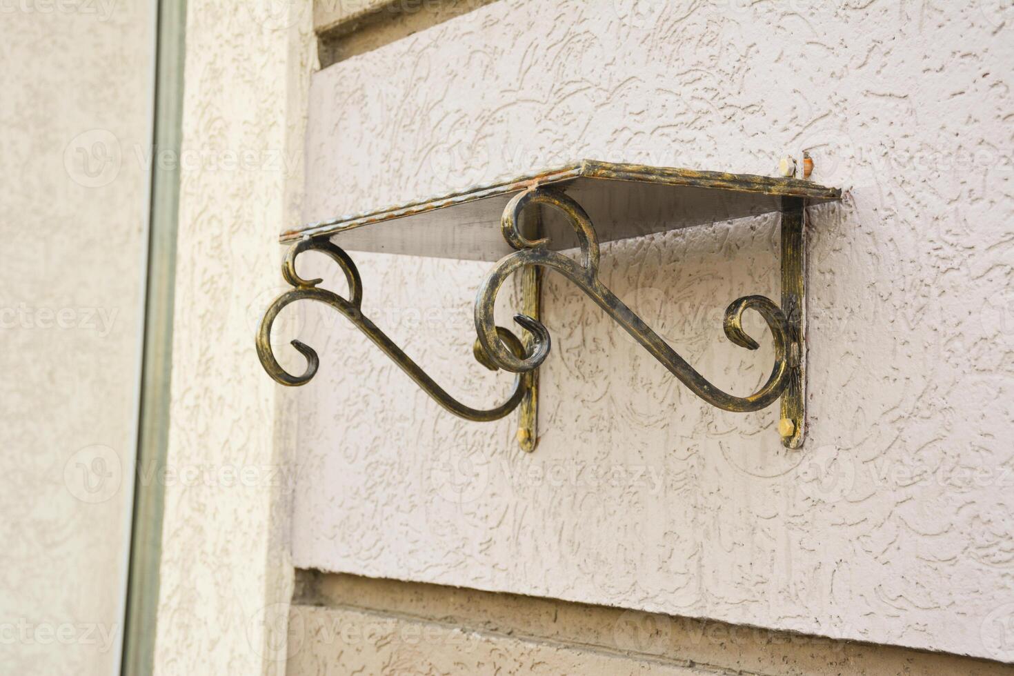 Forged Brackets with a memorial shelve for flowers. Bronze forged shelf with beautiful holders with scrolls and ornaments on the facade of a building. photo
