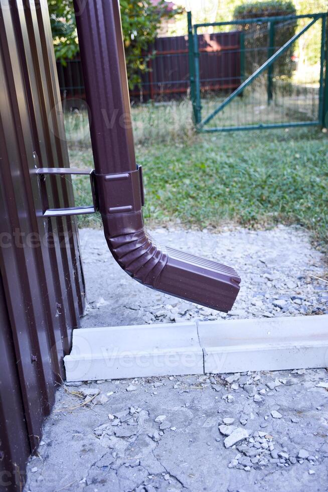A close-up of a brown gutter pipe. The installation that drains water from the roof. Drainage system attached to the house. Guttering system. photo