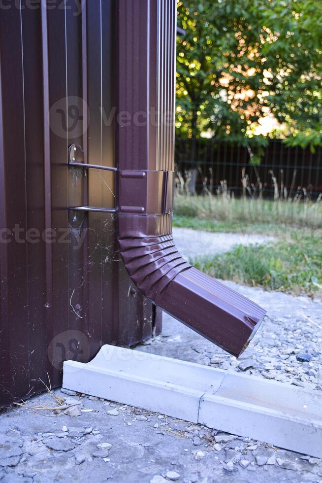 A close-up of a brown gutter pipe. The installation that drains water from the roof. Drainage system attached to the house. Guttering system. photo