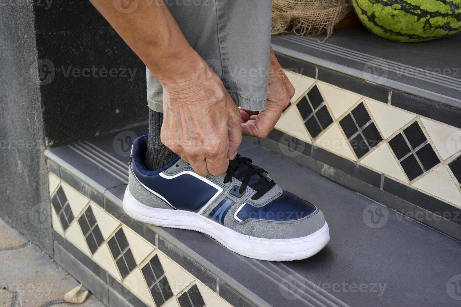 A close-up of hands tying shoelaces on a step of a staircase. An elderly person ties his shoelaces in the city street. photo