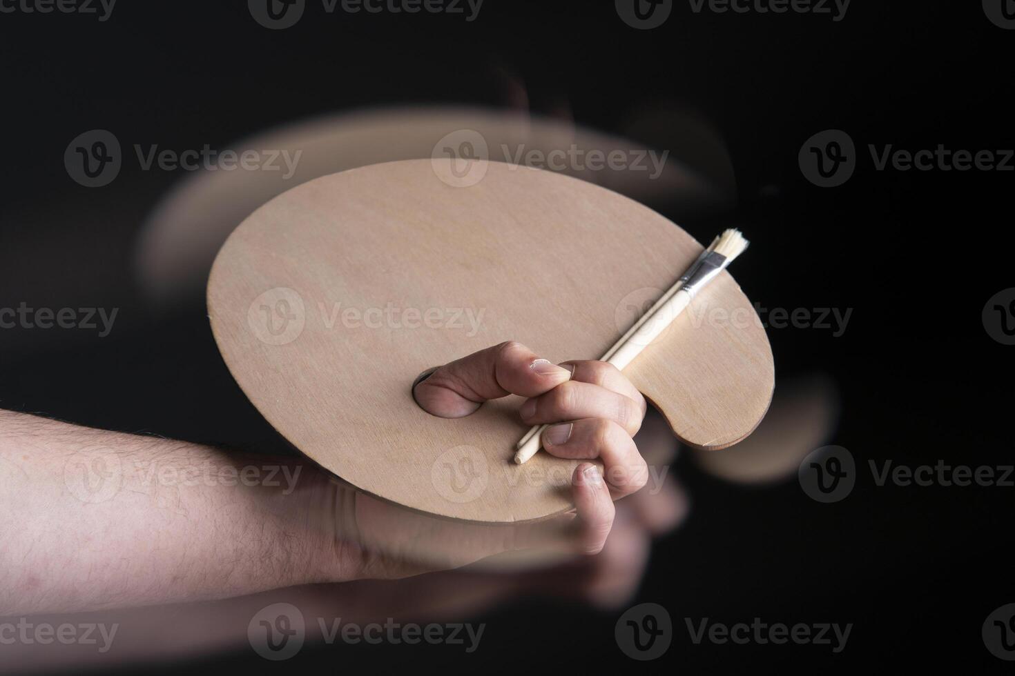 Close up of man's hand holding round wooden palette and paint brushes with motion effect photo