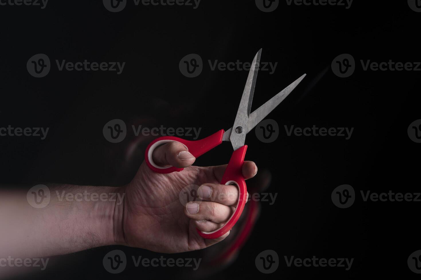 Close up of man's hand holding red handled scissors with motion effect photo