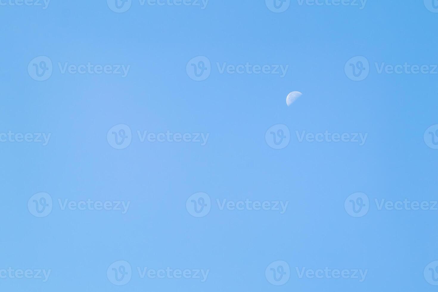 A beautiful crescent moon in the afternoon sky. A crescent moon in daylight against a clear blue sky. photo