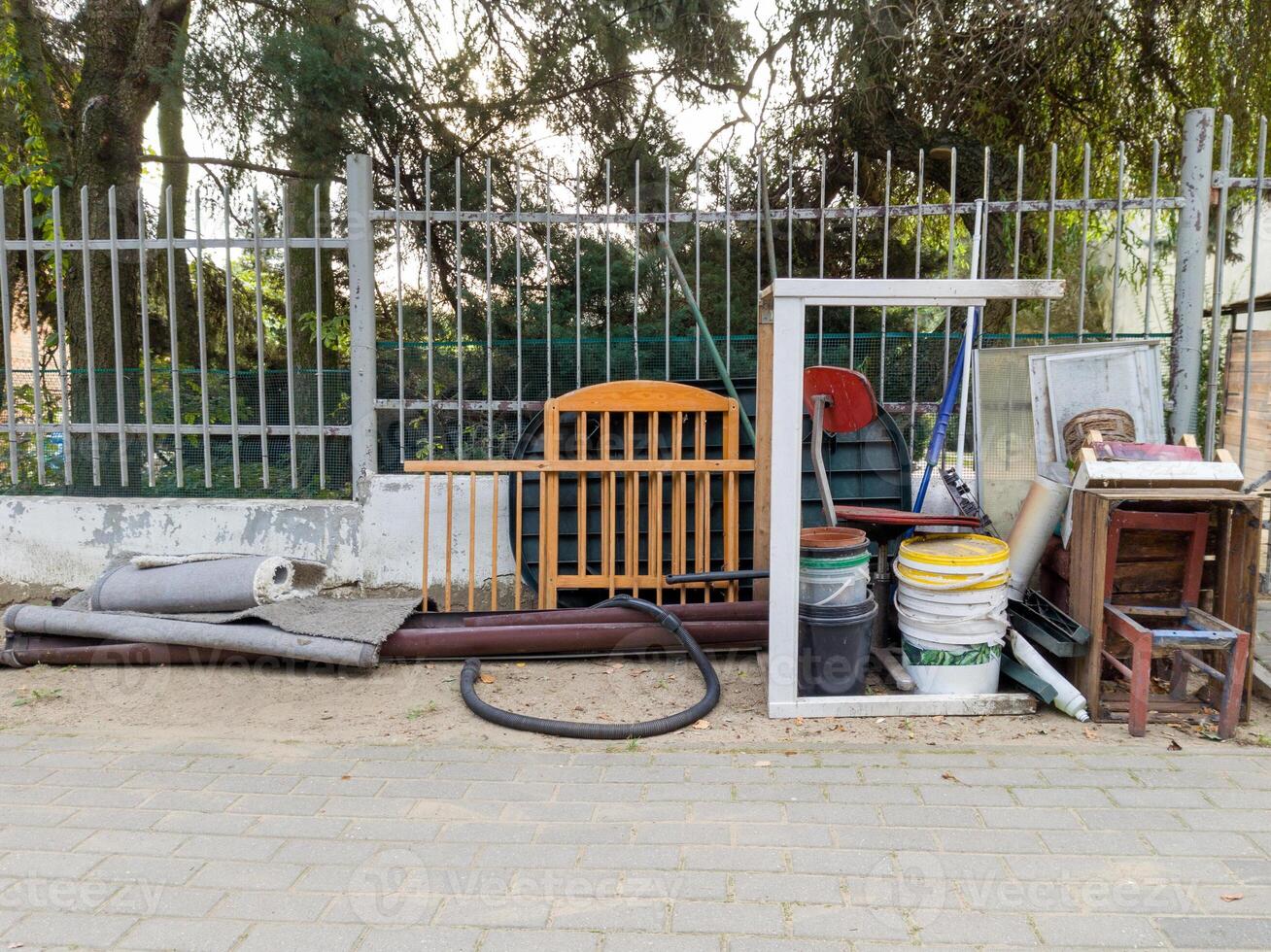 Various discarded items and furniture near a street fence photo
