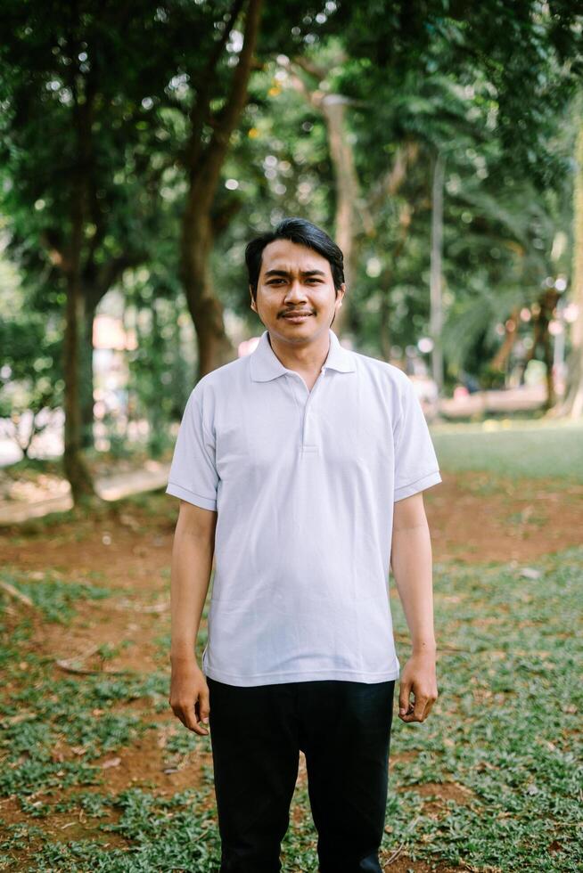 Southeast Asian man standing on an open grassy field in a city square, capturing a moment of calm and space. photo