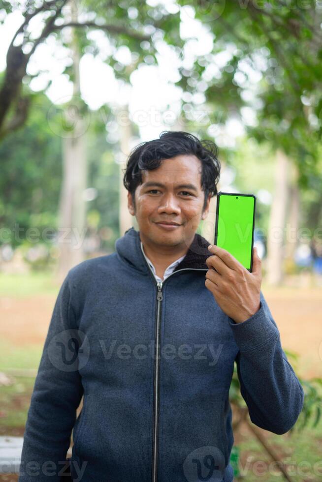Southeast Asian man showing something on his smartphone with a green screen, perfect for customizable content photo