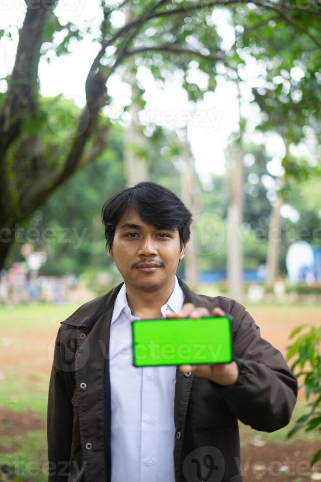 Southeast Asian man showing something on his smartphone with a green screen, perfect for customizable content photo