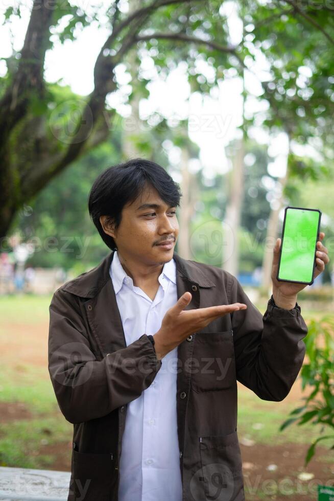 Southeast Asian man showing something on his smartphone with a green screen, perfect for customizable content photo