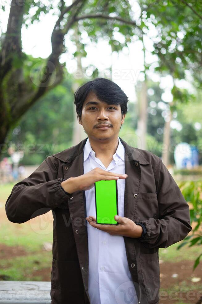 Southeast Asian man showing something on his smartphone with a green screen, perfect for customizable content photo