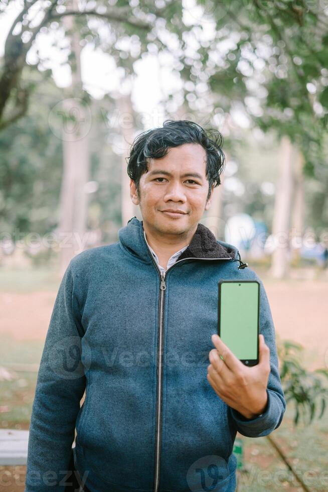 Southeast Asian man showing something on his smartphone with a green screen, perfect for customizable content photo