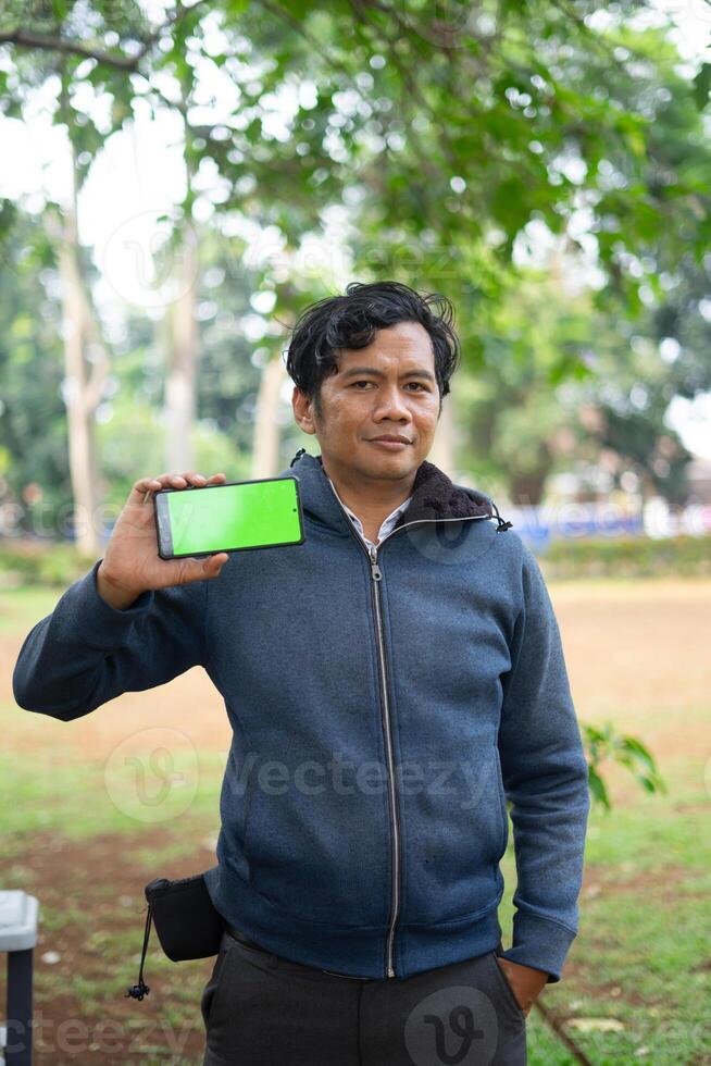 Southeast Asian man showing something on his smartphone with a green screen, perfect for customizable content photo