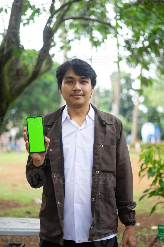 Southeast Asian man showing something on his smartphone with a green screen, perfect for customizable content photo