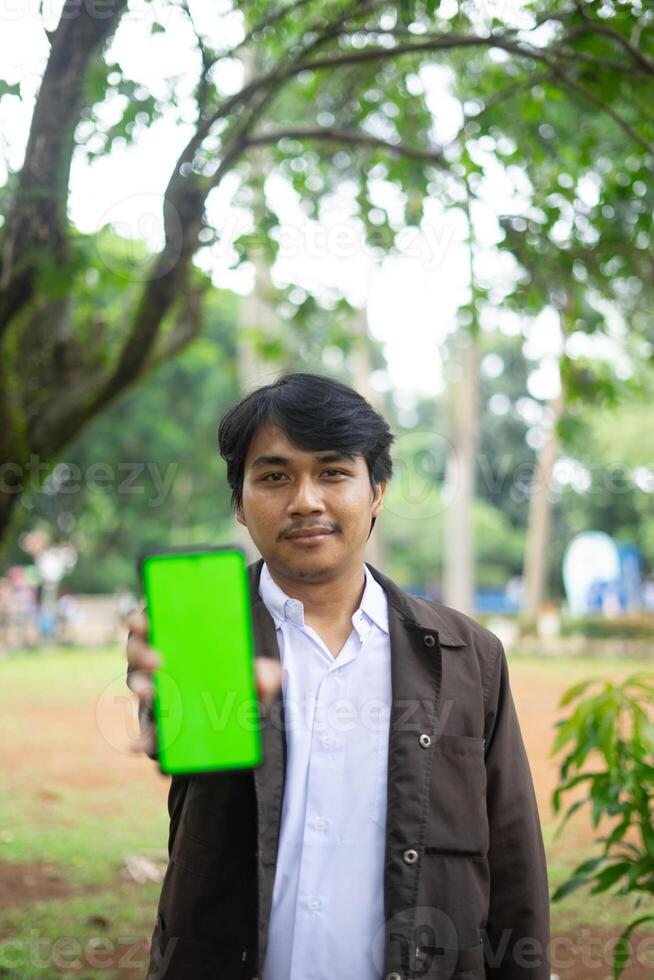 Southeast Asian man showing something on his smartphone with a green screen, perfect for customizable content photo